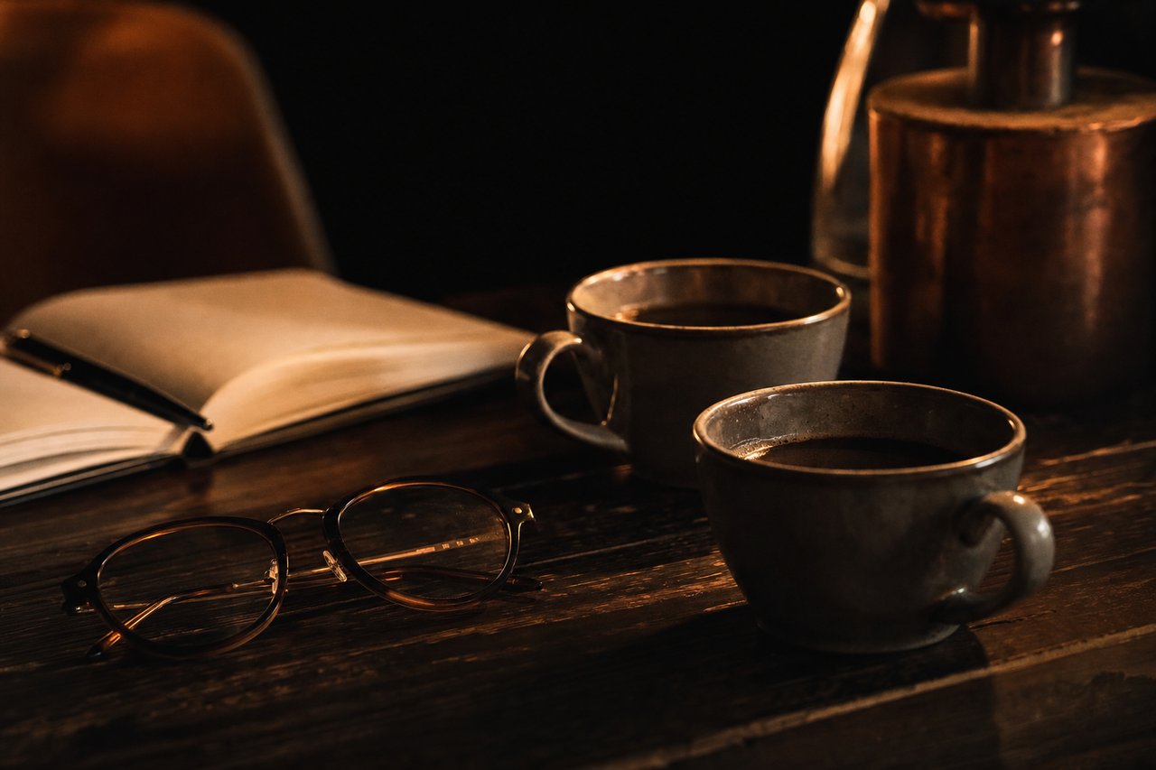 Zwei Kaffeetassen und ein aufgeklapptes Notizbuch mit handschriftlichen Notizen zu einer Singlebörse ab 50 bei Abendlicht